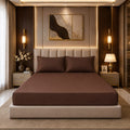 Premium chocolate brown fitted mattress cover with matching pillowcases in a luxury bedroom with gold accents and warm lighting